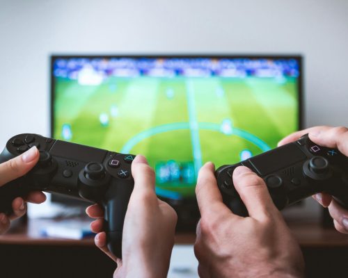 Close-up of hands holding gaming controllers in front of a TV. Engaged in a video gaming session.
