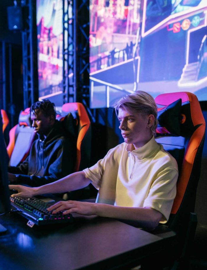 Two young men intensely gaming at an esports event with neon-lit screens.