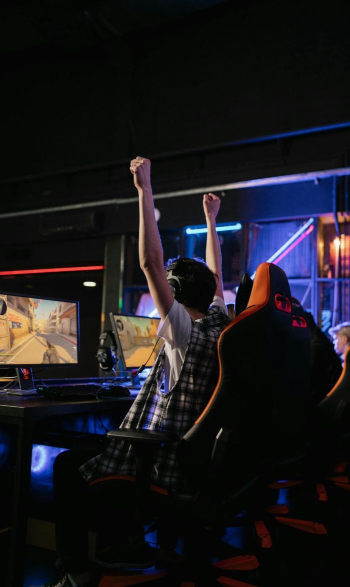 A teenage boy raises his hands in victory while playing video games in an esports arena.