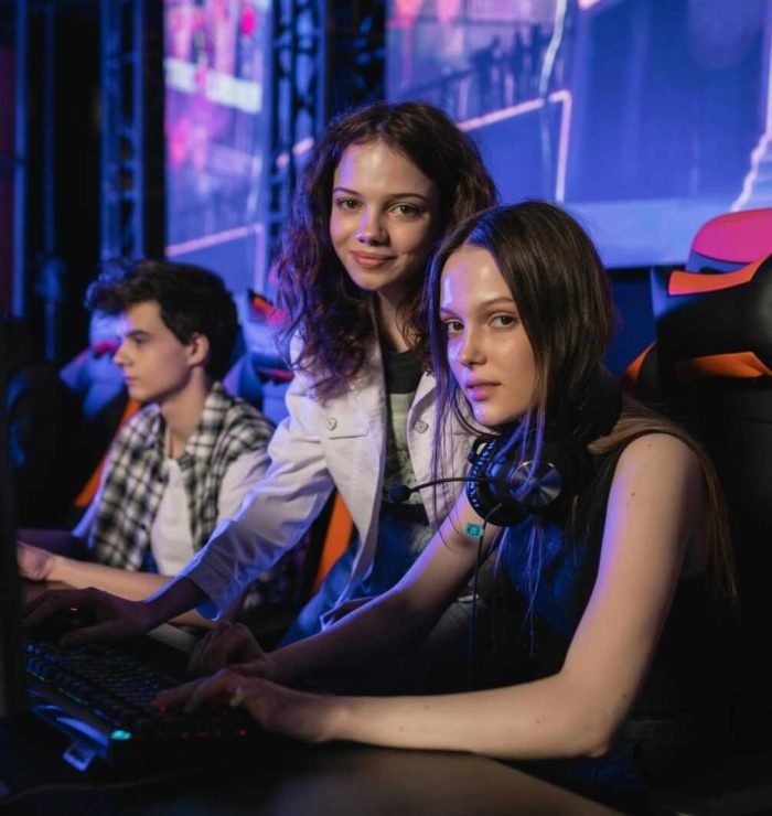 Three teenagers gaming intensely at an esports arena with computers and gaming chairs.