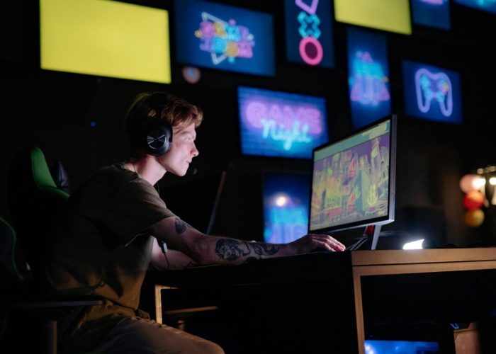 Young gamer engrossed in playing video games with a neon-lit background of multiple screens.